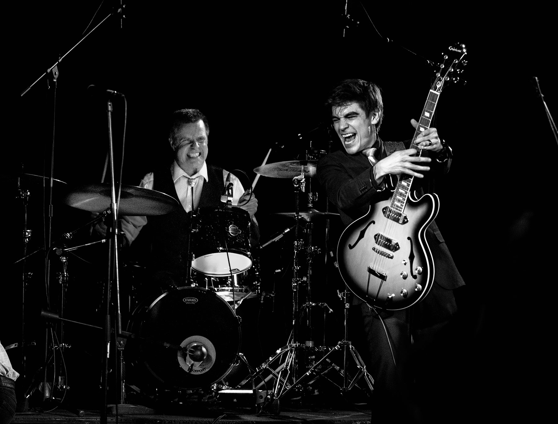 Two musicians, one guitar player, one drummer, on stage performing live.